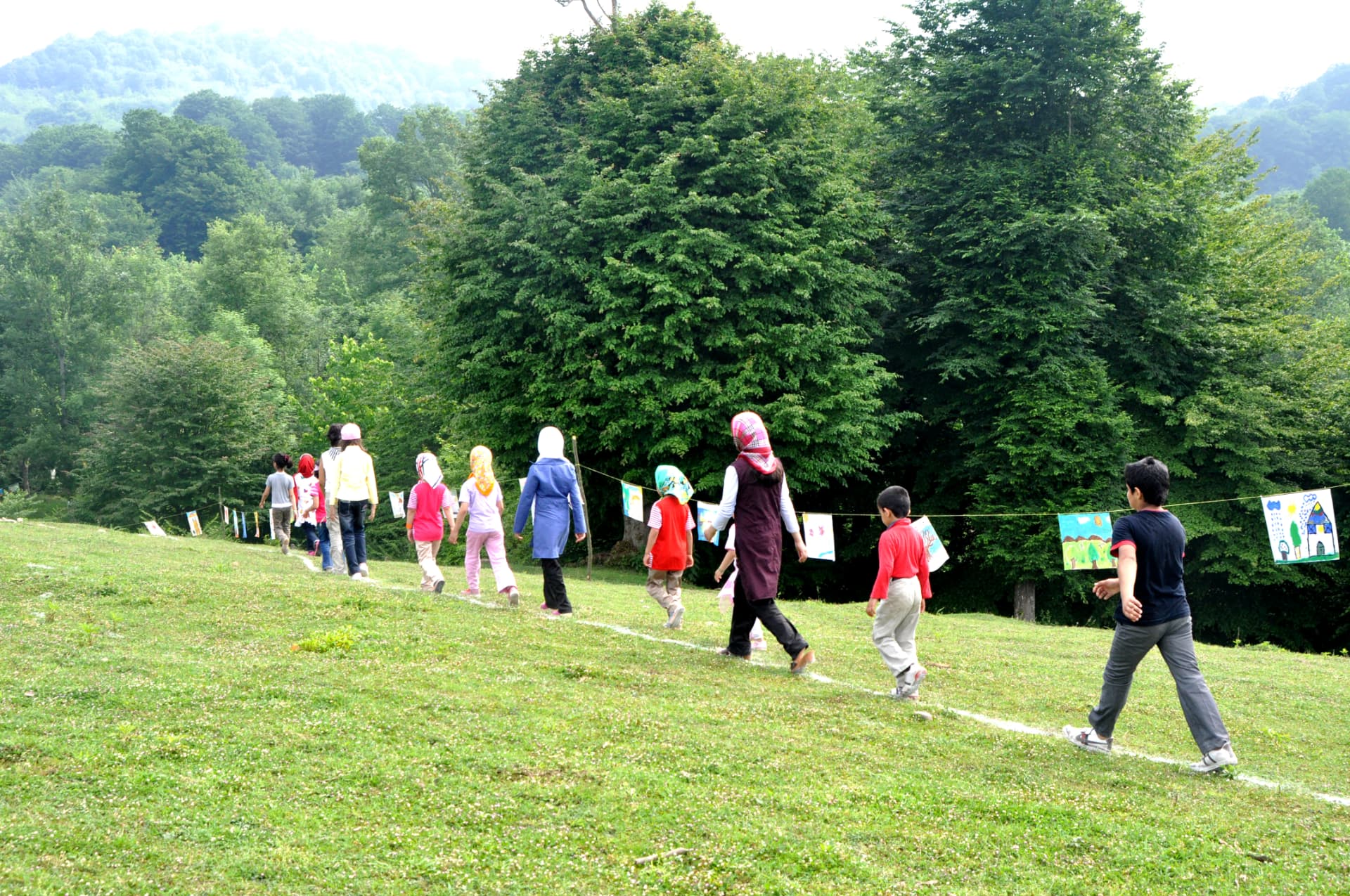 Children walking along a clothesline gallery of paintings in a rural meadow